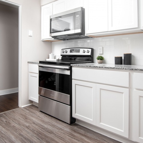 Spacious and well lit kitchen with wood floors and stainless steel appliances. 